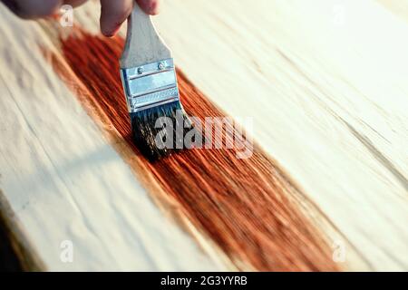 Un cabinettista in funzione tiene in mano una spazzola e dipinge una superficie di legno. Una traccia di vernice su una tavola di legno. Foto Stock