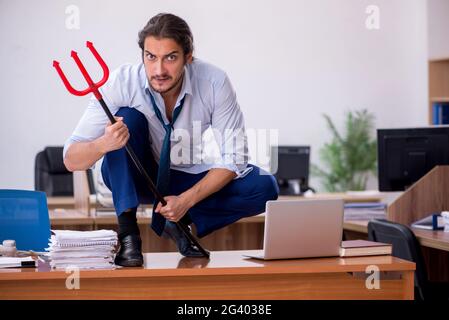 Giovane uomo d'affari diavolo che tiene tridente in ufficio Foto Stock