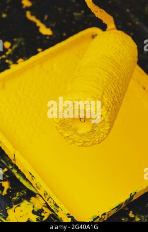 Rullo di vernice con vassoio di verniciatura. Ristrutturazione dell'appartamento. Sfondo di plastica nero. Colore giallo trendy. Primo piano verticale della foto. Foto Stock