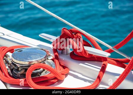 Barca a vela funi ormeggio sul ponte. Corda di yachting di colore rosso allacciata su tacchetto. Catena metallica pesante intorno al verricello, spazio, modello di scheda di crociera. Sailbo Foto Stock