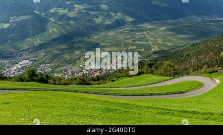 Un tornante su una ripida salita in montagna con il villaggio di Corzes sullo sfondo, Alto Adige, Italia Foto Stock