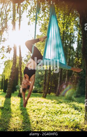 Giovane donna che fa esercizi di yoga antigravitazionale all'aperto. Aero fly fitness Conzept. Foto Stock