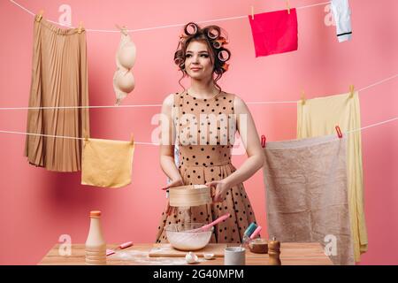 Donna prepara il cibo, setola la farina attraverso un setaccio. Bella casalinga è occupato con le faccende domestiche su uno sfondo rosa. Foto Stock