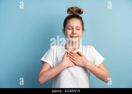 La ragazza teen, sincera e sorridente, mostra un gesto dal cuore, anima. Bella bambina gesturing su una parete di sfondo giallo, copia spazio. Foto Stock