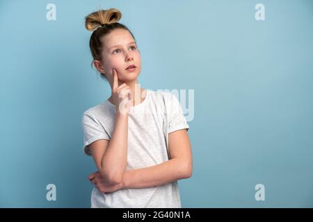 Ragazza adolescente concepita in una T-shirt bianca su sfondo blu. Cute piccola ragazza isolata su sfondo muro vuoto. Foto Stock