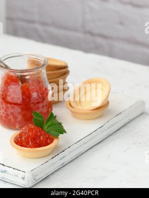 Caviale rosso in un vaso di vetro e tartine rotonde su un tavolo bianco Foto Stock