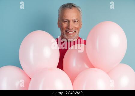 Uomo positivo, allegro con palloncini che posano su sfondo blu parete. Uomo attraente in un maglione luminoso, positivo, allegro uomo con palloncini in posa o Foto Stock
