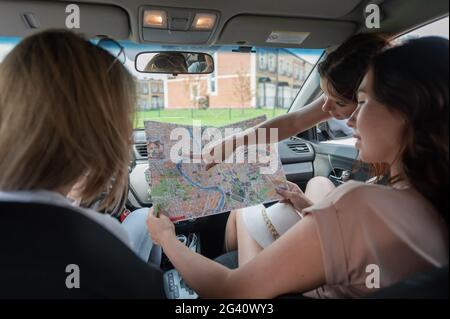 Tre amici e un cane viaggiano in auto. Le donne guardano una mappa cartacea e pianificano un percorso mentre sono in vacanza Foto Stock