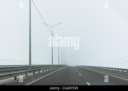 Autostrada invernale. Un paesaggio grigio e desolato con un'ampia autostrada senza auto. Il concetto di cattivo tempo, viaggi indipendenti a lunga distanza, auto-isolo Foto Stock