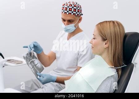 Il dentista comunica con il paziente. Il paziente nella sedia dentale ascolta il consiglio del medico Foto Stock