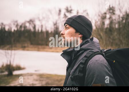 Uomo triste solitario, in piedi con la schiena e guardando il lago ghiacciato nella foresta. Depressione, cattivo umore e pensieri suicidi. Ho bisogno di p Foto Stock