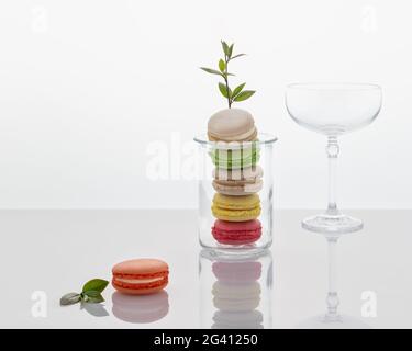 Cibo romantico primaverile ancora vita con dessert francese - macaroon con un'attrezzatura fiorente e un bicchiere da cocktail vuoto su uno sfondo chiaro con un riflesso Foto Stock