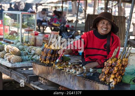 Donna felice con la rana alla griglia ripiena in una bancarella di cibo di strada nel mercato, Oudong (Udong), Kampong Speu, Cambogia, Asia Foto Stock