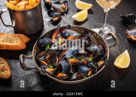 Cozze con vino, limone, pane tostato e patatine fritte Foto Stock