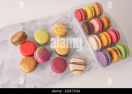 Vista dall'alto dei macaroni francesi in scatola regalo, avvolti in scatola regalo sul piano portapaziente in marmo. Selezione colorata di pasticcini Foto Stock