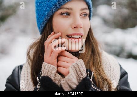 Felice bella ragazza in cappellino sorridente mentre cammina nel parco invernale Foto Stock