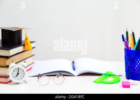 Libri, materiali per la scrittura, occhiali, notebook e sveglia sul desktop. Ritorno a scuola. Concetto di apprendimento e autoistruzione. Foto Stock