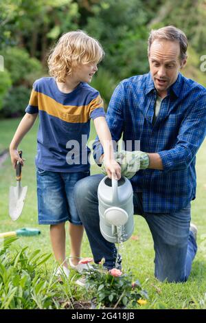 Felice padre caucasico in giardino con figlio, annaffiando piante e giardinaggio insieme Foto Stock