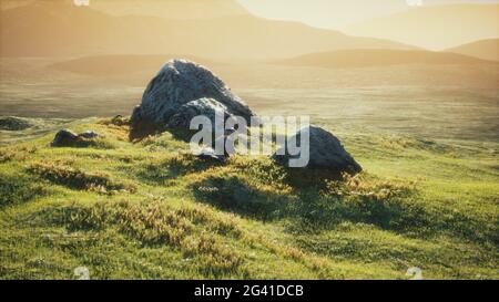 Prato con enormi pietre tra l'erba sulla collina al tramonto Foto Stock