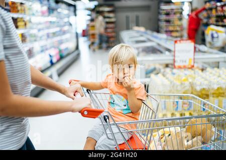 Budva, Montenegro - 17 marzo 2021: Un bambino si siede in un carrello in un supermercato e mangia un bocco. Foto Stock