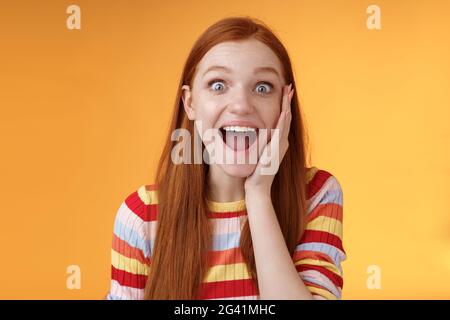 Divertito felice sorridente bella donna rossa gridando felicemente toccare guancia stupita ricevere buone notizie perfette trionfando fe Foto Stock