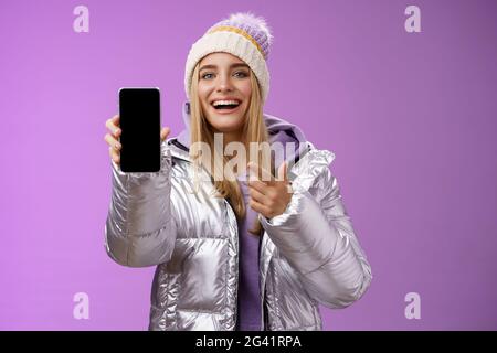 Soddisfatto divertito buon-sguardo bionda ragazza suggerisce lo schermo dello smartphone di Take Look sorridente felice di indicare il telefono cellulare felice ta Foto Stock