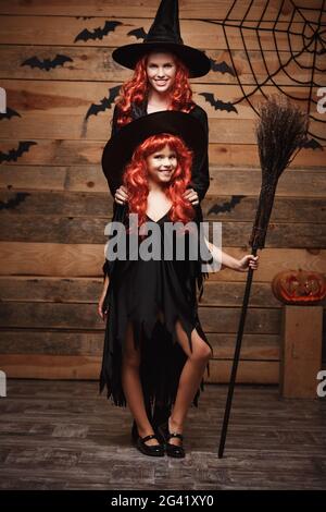 Halloween Concept - bella madre caucasica e sua figlia con lunghi capelli rossi in costumi di strega che celebrano il posin di Halloween Foto Stock