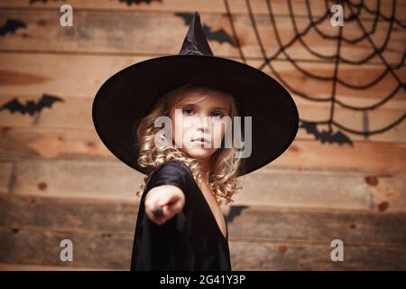 Halloween strega concetto - little witch bambino divertirsi con la bacchetta magica. su bat e spider web sfondo. Foto Stock