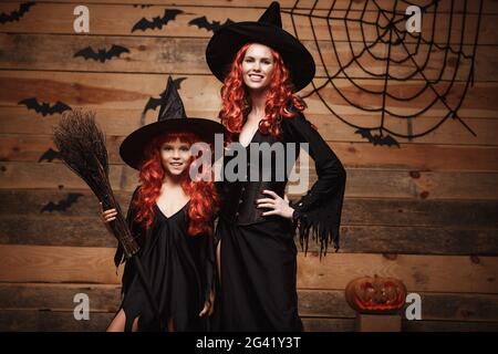 Halloween Concept - bella madre caucasica e sua figlia con lunghi capelli rossi in costumi di strega che celebrano il posin di Halloween Foto Stock