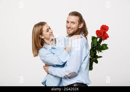 Ritratto di un giovane attraente nascondendo fiori dalla sua fidanzata prima di darle una sorpresa su bianco isolato backgrou Foto Stock