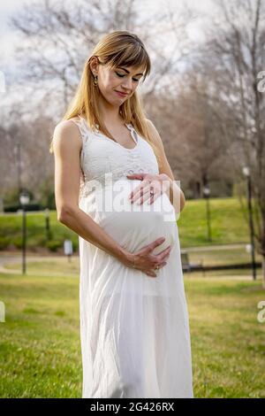 Una meravigliosa donna incinta incandescente posa in un ambiente esterno Foto Stock