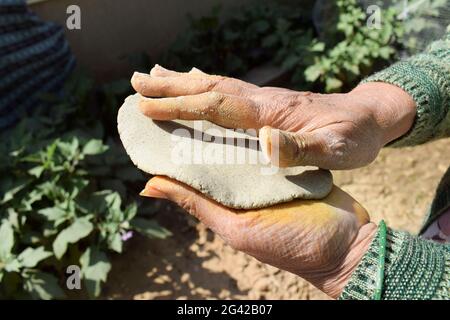 Donna che fa pane piatto indiano o pakistano fatto di miglio perla conosciuto come Bajre ki roti. L'impasto viene appiattito con le mani per formare un cerchio rotondo. Village st Foto Stock