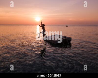 Vista aerea della silhouette di giovane coppia che salta da una piattaforma balneare al tramonto sulla spiaggia di Ong Lang, Ong Lang, Phu Quoc Island, Kien Giang, Vietnam, Come Foto Stock