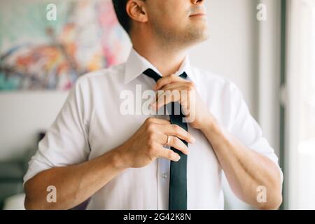 Un uomo si mette e lega una cravatta mentre si prepara per una cerimonia nuziale Foto Stock