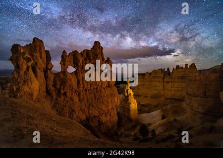 Un hoodoo con piccole finestre e Thor's Hammer contro un cielo notturno con le nuvole e la Via Lattea sotto Sunset Point nel Ryce Canyon National Park, Utah. Foto Stock