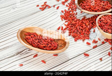 Goji secco aka. Semi di mirtillo in ciotole di legno e versato su scrivania tavole bianche Foto Stock