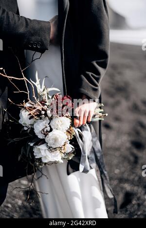 Destinazione Islanda matrimonio. Primo piano del bouquet della sposa, lo sposo abbraccia la sposa in vita. Foto Stock