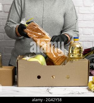 Donna in un maglione grigio sta imballando il cibo in una scatola di cartone, il concetto di assistenza e di volontariato Foto Stock