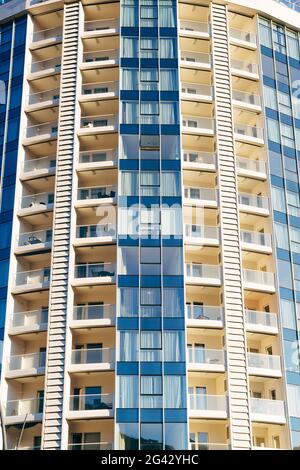 Alto edificio a più piani in blu e beige con balconi con vetri. Foto Stock