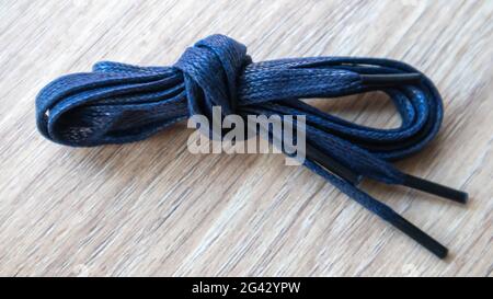 Un soggetto di lacci piatti blu scuro con punte sottili per le scarpe arrotolate e isolate su uno sfondo di legno. Accessorio elegante Foto Stock