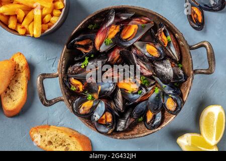 Cozze in padella, con patatine fritte, pane tostato e limone Foto Stock