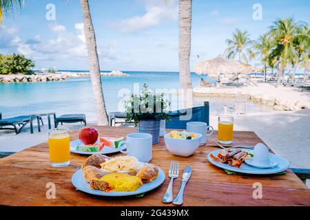 Colazione su un tavolo vicino alla spiaggia che si affaccia sull'oceano, mare dei Caraibi con tavolo per la colazione con succo d'arancia e caffè cr Foto Stock