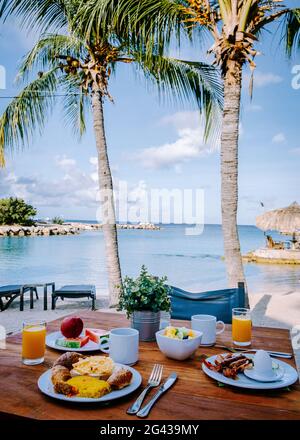 Colazione su un tavolo vicino alla spiaggia che si affaccia sull'oceano, mare dei Caraibi con tavolo per la colazione con succo d'arancia e caffè cr Foto Stock