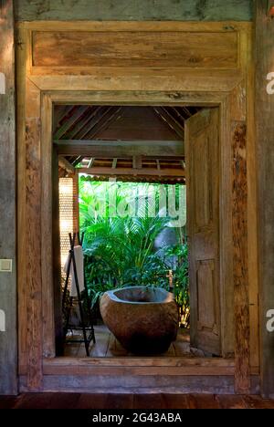 Vasca da bagno in pietra posta all'interno di un bagno aperto, in una vecchia casa di legno situata nella giungla. Bali, Indonesia. Foto Stock