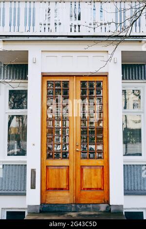 Porte in legno con vetro soffiato nell'edificio con finiture bianche e finestre in plastica con persiane, sotto un grande balcone. Foto Stock