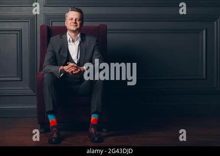 Ritratto di un uomo adulto medio sorridente in tuta grigia e calze multicolore colorate che guardano la fotocamera con spazio per la copia Foto Stock