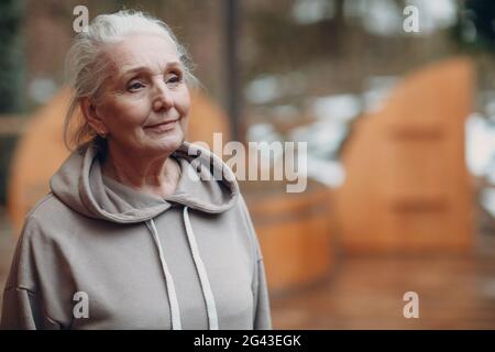 Ritratto di donna anziana con capelli grigi maturi in felpa con cappuccio all'aperto. Foto Stock
