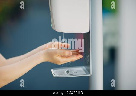 Bambino bambino bambino bambino uso automatico dispenser di gel di alcool spruzzando sulle mani macchina igienizzante disinfettante antisettico, nuova vita normale Foto Stock