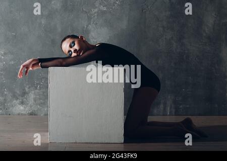 Giovane ragazza professionista ginnastica donna ginnastica ritmica rilassante con cubo bianco in studio Foto Stock