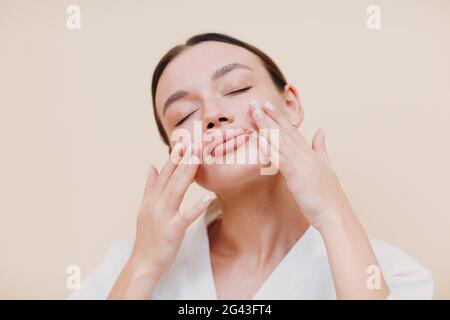 Giovane donna che applica la crema bianca cosmetica sul suo viso Foto Stock